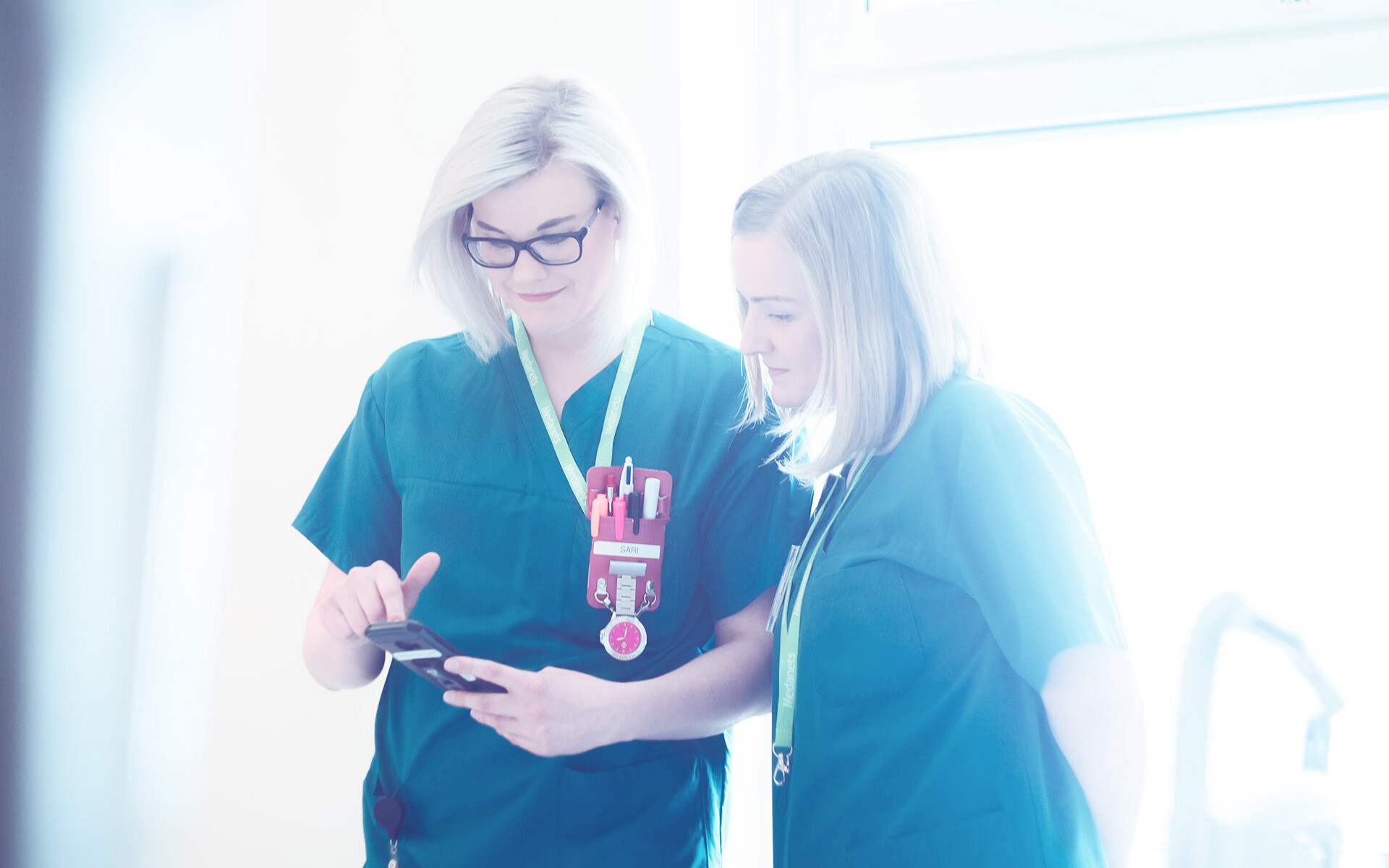 Kaksi sairaanhoitajaa katsoo tietoja kännykän näytöltä.